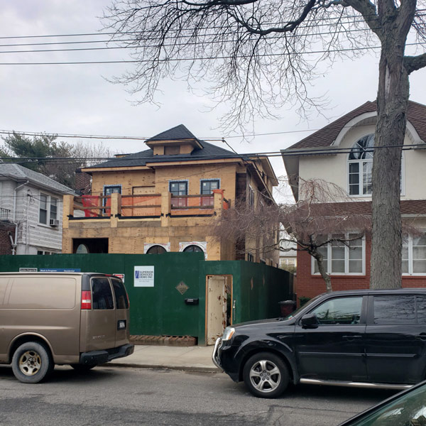 A house with a spacious brown front porch and a car parked in front of it.