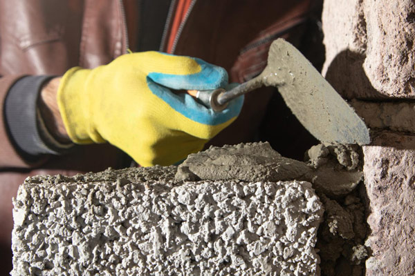 Person in yellow glove using hammer to put cement into wall.